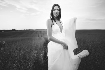 Fototapeta na wymiar beautiful and young bride in white dress standing in a field