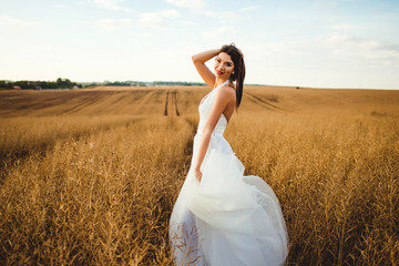 Fototapeta na wymiar beautiful and happy bride in white dress standing in a field
