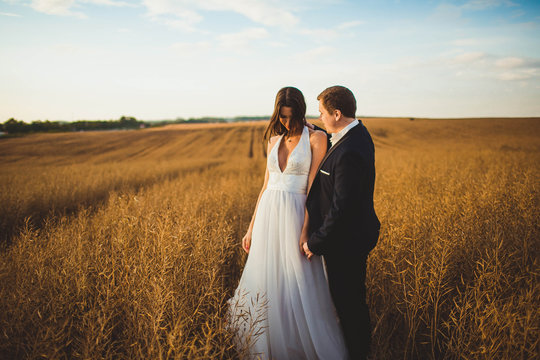 happy and young bride and groom standing in a field