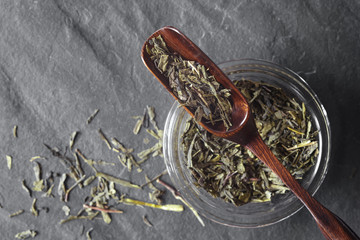 Glass jar with tea and wooden spoon on the dark stone background top view