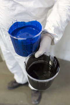 The Netherlands, Utrecht. Inside the factory of a Dutch design furniture brand.  A painter holding two buckets of paint. One blue and one black.