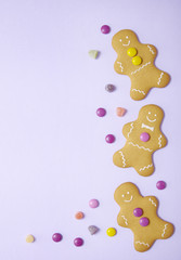 Hand decorated gingerbread men on a pastel purple background with candy and blank space at side