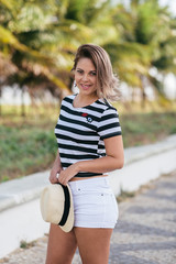 Fashionable girl photo. Marine style. Beautiful blonde woman having fun on vacation in stripped t-short and summer hat on the beach