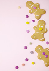 Hand decorated gingerbread men on a pastel pink background with sweets arranged to form a page frame