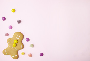 Hand decorated gingerbread men on a pastel pink background with sweets and empty space at side