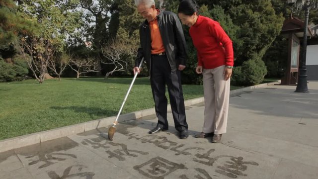 MSD TD Elderly couple writing Chinese calligraphy with water on pavement in park/ Beijing, China