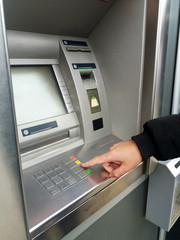 Man's using the ATM machine with cash cards. Close-up of hand entering PIN/pass code on ATM/bank machine keypad.