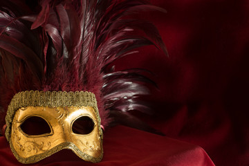 goldene Augenmaske mit roten Federn vor dunklem Hintergrund