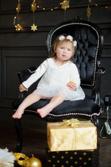 Little ruddy girl sits in a beautiful chair and eats cookies.