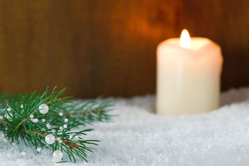 Christmas decoration: branch of Christmas tree with white pearls and burning candle in snow