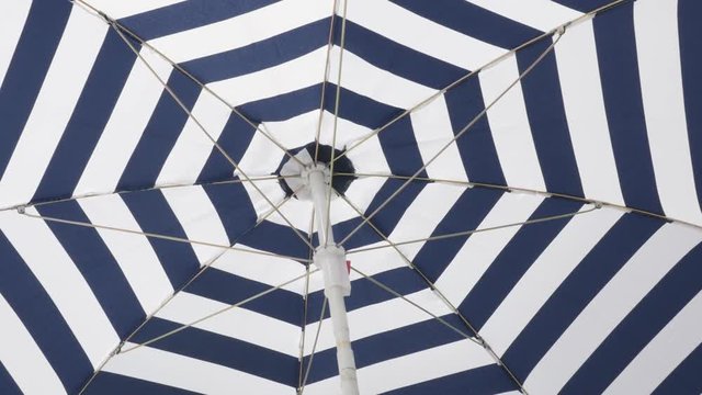 Under striped fabric of shade umbrella made for protection from the sun 4K 2160p 30fps UltraHD footage - Beach blue parasol on the beach moving on the wind 3840X2160 UHD video 