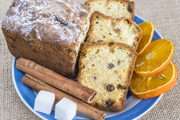sliced cake with raisins, slices of orange, canela on blue plate on sackcloth background