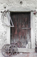 Fototapeta na wymiar Rural historic door, two saws and two wooden spoked wheels
