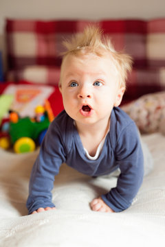Little baby boy with spiky hair crawling on bed.