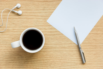 Workplace background with a cup of coffee on wooden desk, white paper, a pen and earpiece
