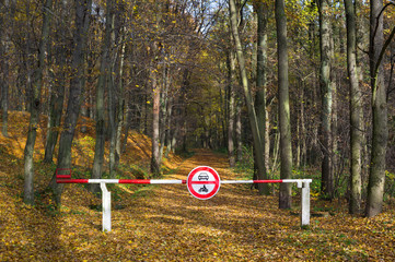 Fototapeta na wymiar Gate on the road to the wood. Traffic barrier for stopping cars and motorbikes to enter into the forest. Autumn will fallen yellow leaves