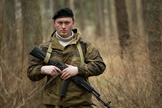 a military man in the woods with a Kalashnikov assault rifle, autumn forest with no leaves, green form