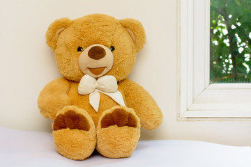 Obraz premium Teddy bear sitting on a bed near a window.