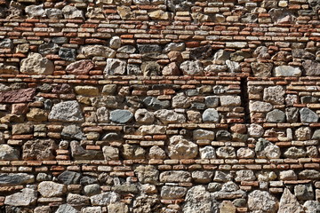 Detail of a horizontal stony wall made of thin and thick rows of bricks and stones