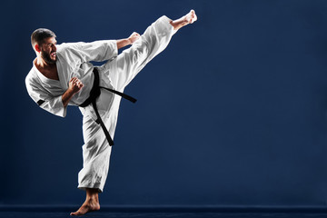 Karate man in a kimono hits foot on a blue background - obrazy, fototapety, plakaty