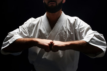 Karate man in a kimono holding fists together on a black background