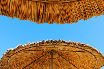 Beach umbrellas made of straw at blue sky background