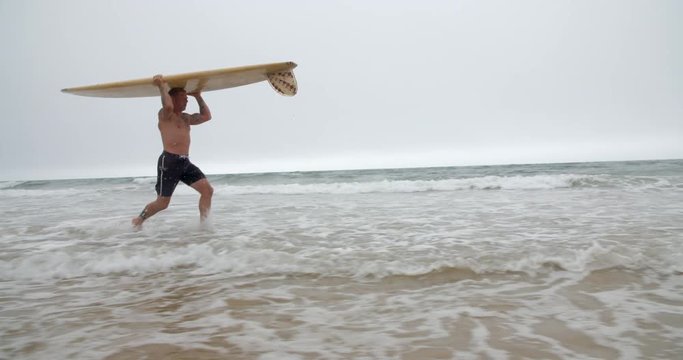 Mature Surfer runs out of the Ocean Waves.