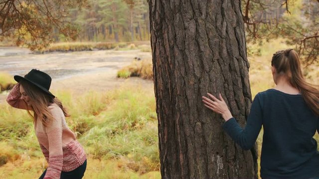 Girls play tag in the autumn forest. One girl in nice hat. Girls have fun and laughing 
