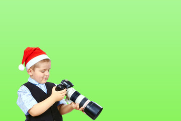 On a green background a little photographer in cap of Santa Claus
