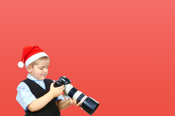 On a red background little photographer in cap of Santa Claus