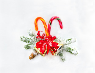 Christmas decoration. Christmas candy canes, branch christmas tree, cone spruce, christmas bells and berry on snow. Top view, flat lay