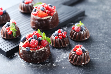 Sweet chocolate cakes with berries on black wooden table