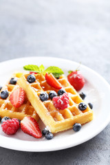 Homemade waffles with berries in plate on grey table