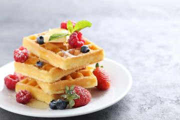 Homemade waffles with berries in plate on grey table