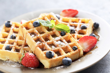 Homemade waffles with berries in plate on grey table