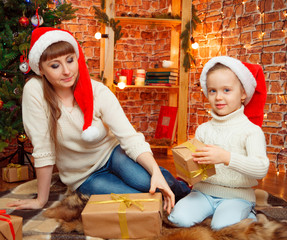 Happy mother, young woman in red santa hat together with her little daughter, cute kid girl, sitting on the floor