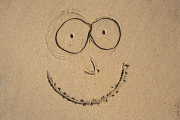 A smiley face drawn in the sand on a beach using seaweed