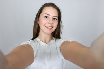 Fototapeta na wymiar Selfie time. Portrait of a pretty smiling woman standing over gray background and looking at camera
