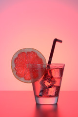 Fresh cocktail with grapefruit, ice and striped drinking straw on a red background.