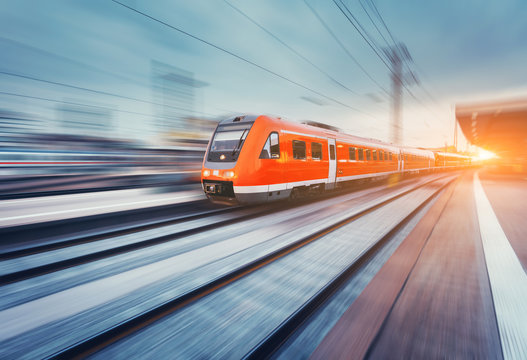 Fototapeta Modern high speed red passenger commuter train in motion at the railway platform at sunset. Railway station. Railroad with motion blur effect. Industrial landscape with train. Vintage toning