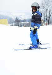 Fototapeta na wymiar Child boy skiing in mountains. Active teenager kid with safety helmet and goggles. Ski race for young children. Winter sport for family. Kids ski lesson in alpine school. Young skier racing in snow