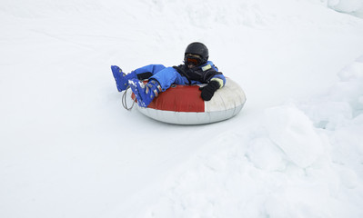 Fototapeta na wymiar A child boy (wearing ski helmet) having fun sledding on a tube in the snow. 