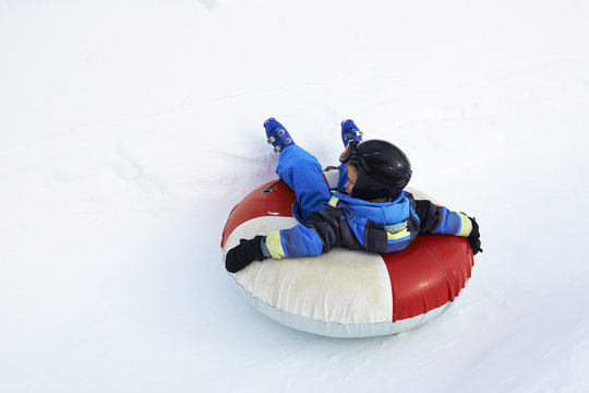 A child boy (wearing ski helmet) having fun sledding on a tube in the snow.
