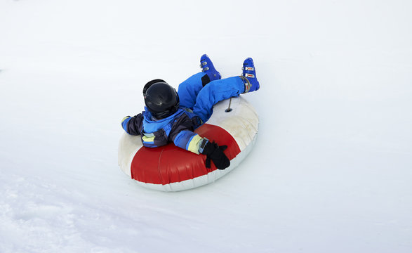 A child boy (wearing ski helmet) having fun sledding on a tube in the snow.

