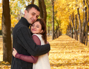 Fototapeta premium romantic people, happy adult couple embrace in autumn city park, trees with yellow leaves, bright sun and happy emotions, tenderness and feelings