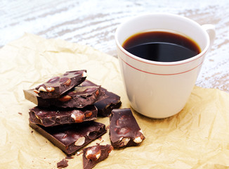 Dark chocolate with nuts and a mug of black coffee on crumpled paper on an old wooden background