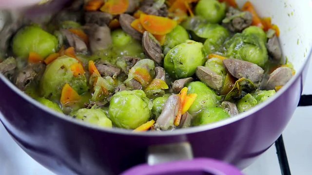 Process of cooking chicken hearts with Brussels sprouts- mixing the ingredients in a pan and cover closing
