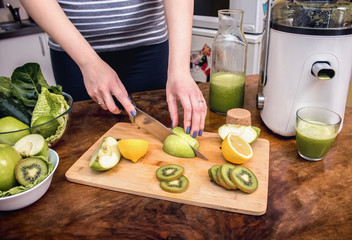 Juicing - woman making apple and green vegetable juice using juicer machine at home in kitchen....