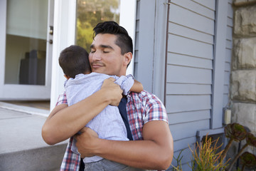 Fototapeta premium Father Hugging Son Sitting On Steps Outside Home