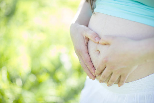 Soft image of pregnant woman embracing her belly and shaping hands in a heart